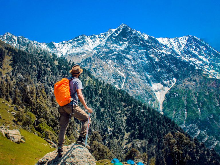 Man exploring breathtaking mountain scenery with snow-capped peaks under a clear blue sky.